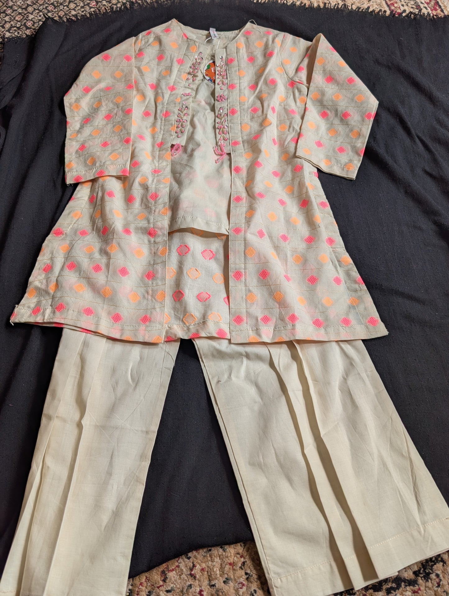 Girls light cream jacket with pink, orange, and gold geometric embroidery and beaded trim, layered over a solid off-white tunic and matching pleated wide-leg trousers,
