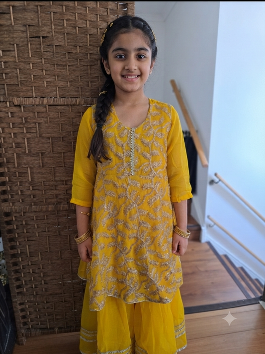 Girl's vibrant yellow traditional ethnic outfit featuring frock intricate gold embroidery across the tunic and matching bottoms gharara.